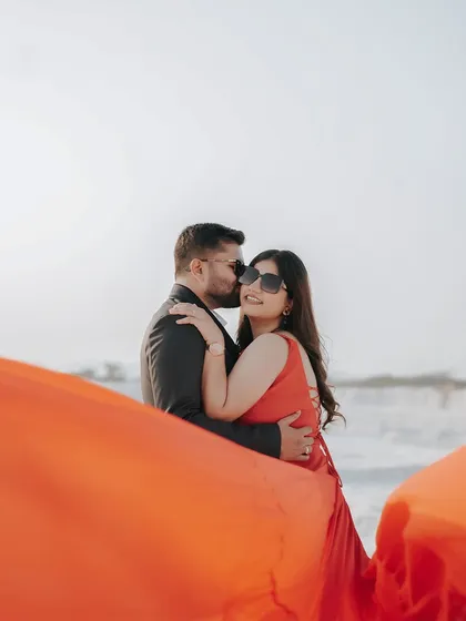 A sweet and candid moment as the groom kisses his bride's cheek, with the dramatic red fabric of her dress filling the foreground.