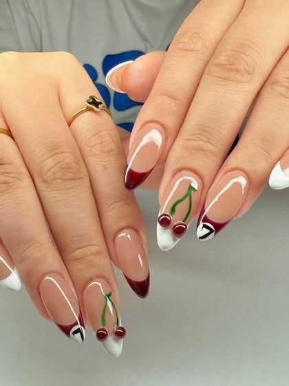 A fun and unique French manicure with a mix of white and deep red tips, accented with cute cherry art.