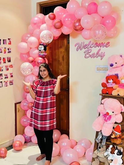 A sweet and simple 'Welcome Baby' home decoration in all pink. The setup features a balloon arch over a doorway and a ladder decorated with pink teddy bears.