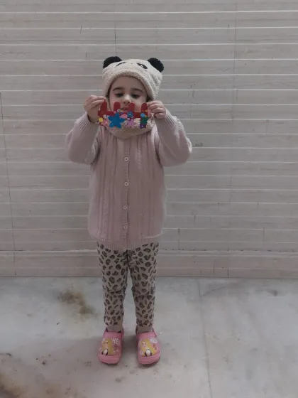 A proud little girl holding up her colorful popsicle stick craft. This activity helps with color recognition, patterns, and fine motor skills.