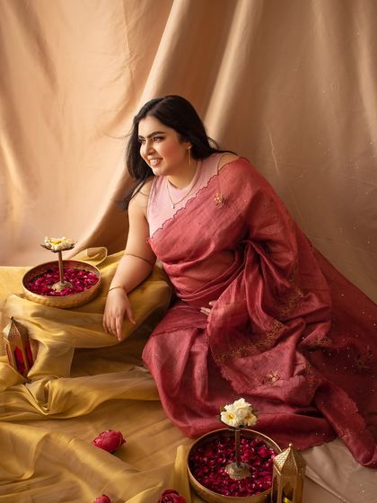A candid and happy solo portrait of the mother-to-be in her saree, surrounded by traditional decor like brass bowls and flower petals.