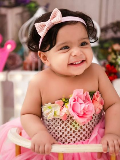 A close-up of a happy one-year-old. Her bright smile and the festive 'ONE' sign in the background perfectly capture the spirit of a first birthday celebration.