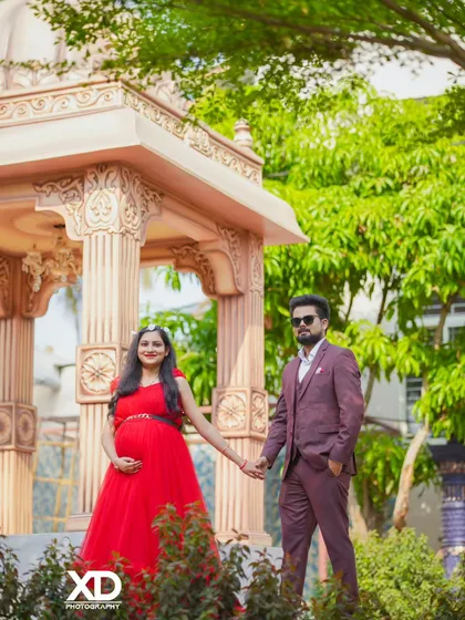 A stylish couple holding hands in a beautiful garden with an elegant gazebo in the background.