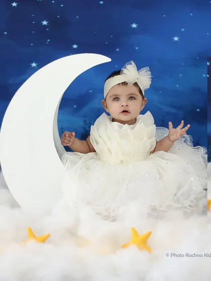 A little angel in a beautiful white dress sits on our moon prop against a starry night sky backdrop.