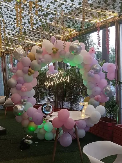 A simple circular balloon arch with a neon sign, set up in a cafe for a birthday celebration.