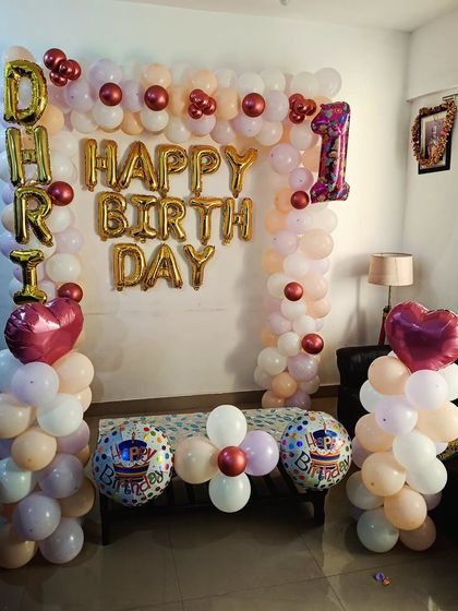 A first birthday decoration with balloon pillars and an arch in pastel colors, with the name 'DHIRI' in foil letters.