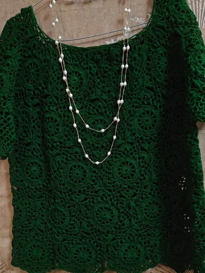 The green lace top styled with a simple pearl necklace. The classic scoop neckline and elegant drape make it a piece that can be dressed up or down for any occasion.