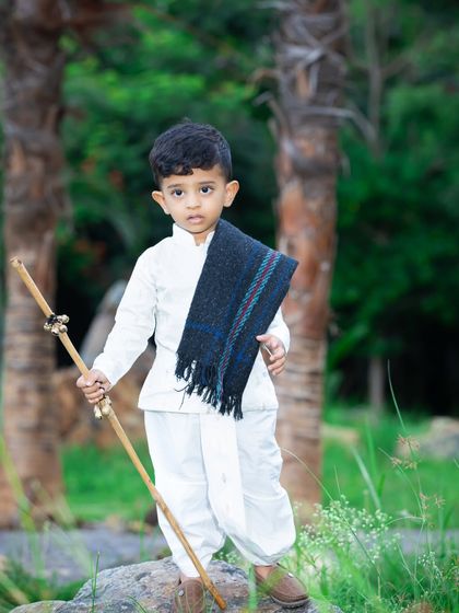 A striking outdoor portrait of a young boy in a traditional dhoti and shawl, holding a wooden staff.