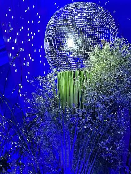 A close-up of a disco ball centerpiece from the 65th birthday party. The shimmering ball sits atop a cloud of baby's breath, perfectly capturing the event's elegant and celebratory "starry night" theme.