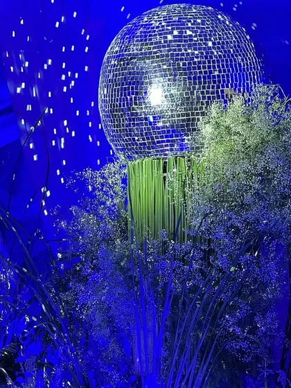 A close-up of a disco ball centerpiece from the 65th birthday party. The shimmering ball sits atop a cloud of baby's breath, perfectly capturing the event's elegant and celebratory "starry night" theme.