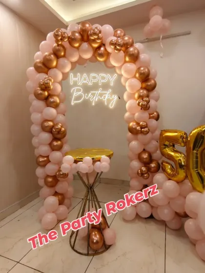 A beautiful balloon arch in pink and rose gold for a 50th birthday, complete with a cake table and foil number balloons. A perfect setup for a home celebration.