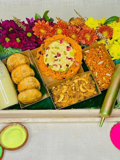 Our exclusive Holi gifting hamper, bursting with color and traditional flavors. It features Ghewar, Kachoris, and Thandai, beautifully arranged with fresh flowers.