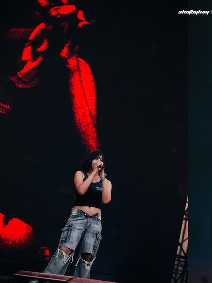 A wide shot of Kim the Beloved on the massive Rolling Loud stage, with abstract red visuals on the screen behind her. This photo shows the artist in the context of the large-scale production.