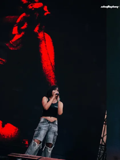 A wide shot of Kim the Beloved on the massive Rolling Loud stage, with abstract red visuals on the screen behind her. This photo shows the artist in the context of the large-scale production.