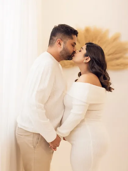 A romantic kiss shared between the expecting parents, captured in a cozy, sweater-weather themed shoot.