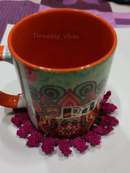 A single magenta floral coaster, showing the beautiful texture of the crochet stitches.