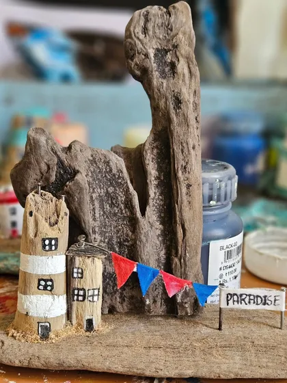 A work-in-progress shot of another driftwood piece, this one celebrating a little slice of paradise. You can see the unpainted wood and the tiny details, like the hand-painted banner, that come together to create these miniature scenes.