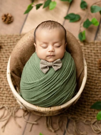 An overhead shot of the baby in a green swaddle and bowtie, nestled in a basket.