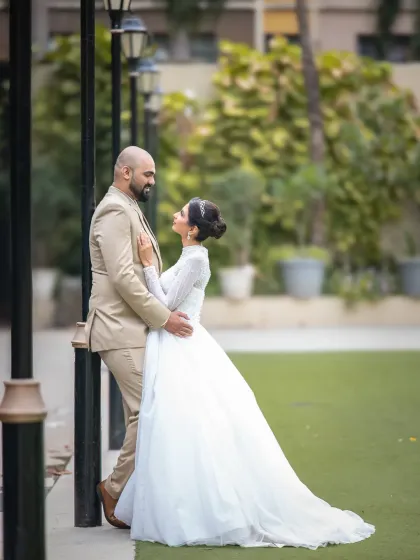 A beautiful, full-length wedding portrait in a garden setting. The bride looks up at her groom, creating a sense of connection and admiration.