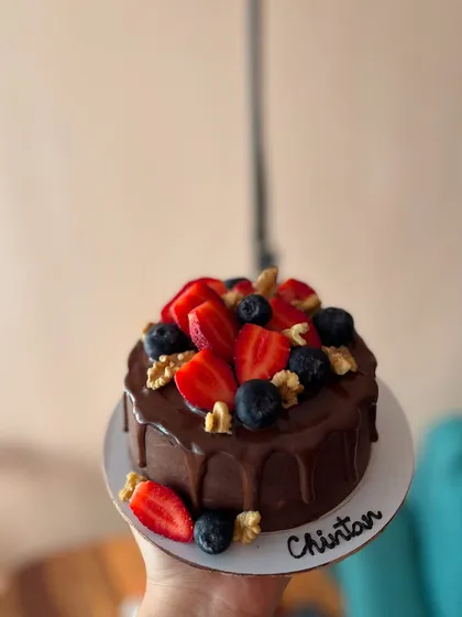 A mini chocolate drip cake topped with fresh strawberries, blueberries, and walnuts. It's a small cake packed with rich flavors.
