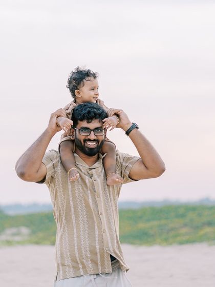 A father and son on the beach, the son perched on his dad's shoulders. A beautiful moment against the backdrop of the sea.