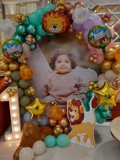 A personalized photo backdrop for a first birthday, framed with a jungle-themed balloon arch and a light-up number '1'.