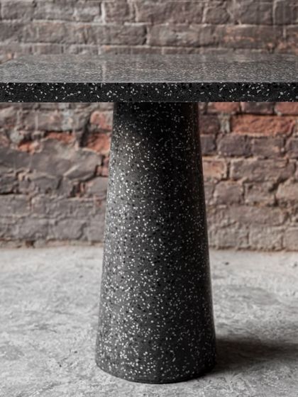 A beautiful and robust terrazzo cafe table with a solid pedestal base. Its dark, speckled finish provides a durable and stylish surface perfect for high-traffic commercial environments like cafes and restaurants.
