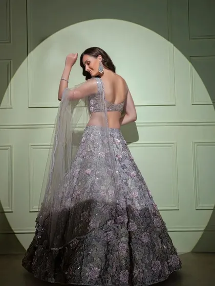 An ethereal ombre lehenga with 3D floral appliqué. The design transitions from a light, silvery grey to a deep charcoal, creating a unique and dramatic effect.