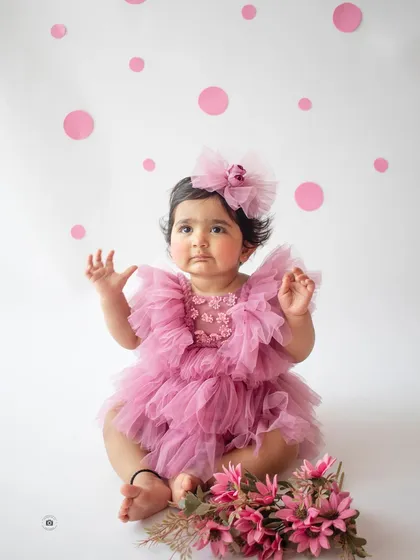 A sweet portrait of a one-year-old girl in her pink birthday dress, sitting with a bouquet of flowers.