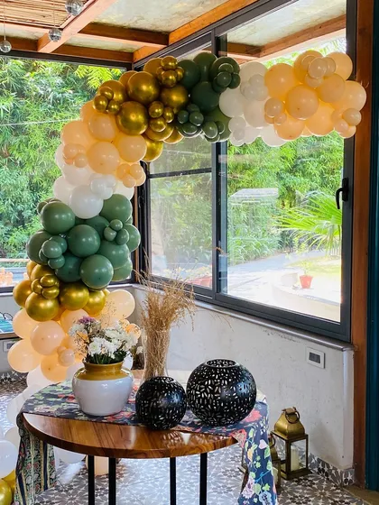 A full view of the olive green and peach balloon arch over a decorated table.