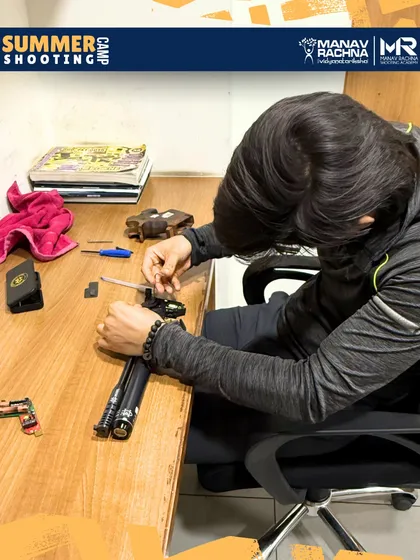 Our summer camps offer a deep dive into the science of shooting. Here, a young athlete is seen servicing his air pistol, learning about trigger velocity and weight adjustments under expert supervision.
