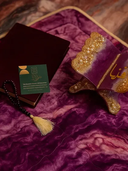 A closer look at the details of this purple and gold prayer set. It includes a personalized Quran holder, a velvet Quran box, and a tasbeeh, all set against a plush, quilted purple prayer mat.