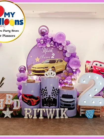 A cool Cars-themed second birthday party. The purple decor features a yellow sports car, Lightning McQueen, and a large light-up number '2'.