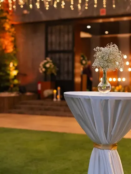 A cocktail table with a simple baby's breath arrangement, set against the warm glow of the evening reception.