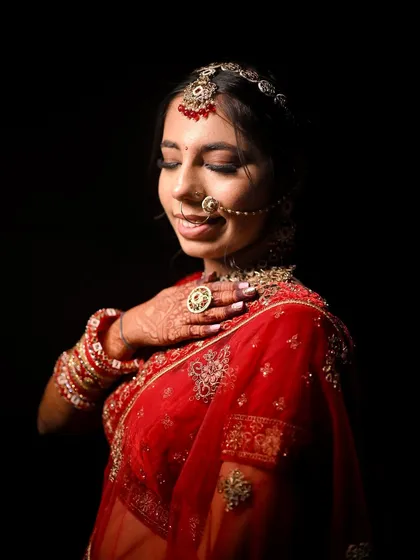 A dramatic portrait with a black background that makes her red outfit and glowing makeup pop. The soft smokey eyes and gentle smile create a captivating image.