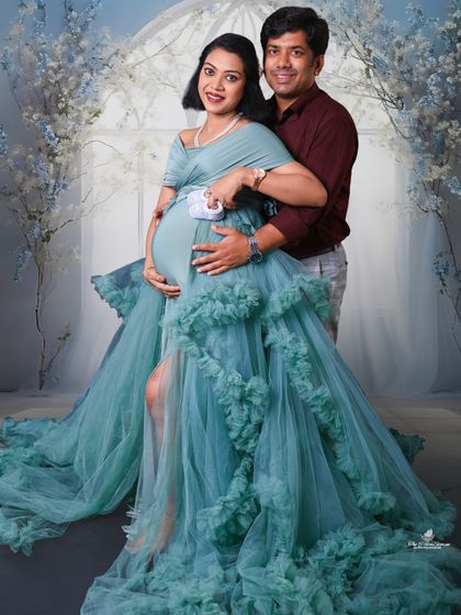 A lovely couple's portrait against a dreamy, light-blue floral arch. They hold a pair of tiny baby shoes, a classic symbol of the new life they are awaiting.