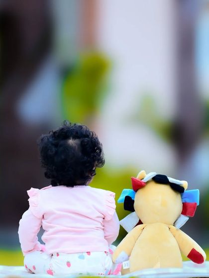 A shot from behind of a baby and their teddy bear, looking out at a park. A sweet, contemplative moment.