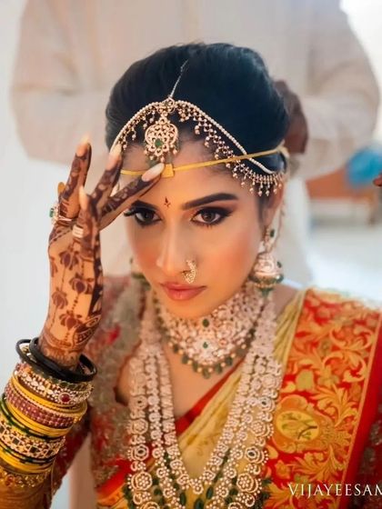 A close-up of a South Indian bride getting ready, her stained hand adjusting her matha patti.