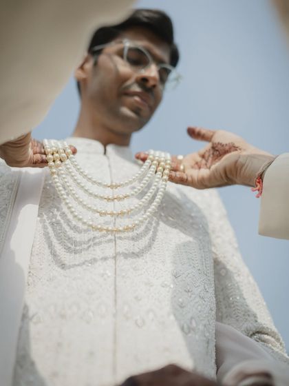 A detail shot focusing on the groom's layered pearl necklace, an essential part of his royal wedding look.