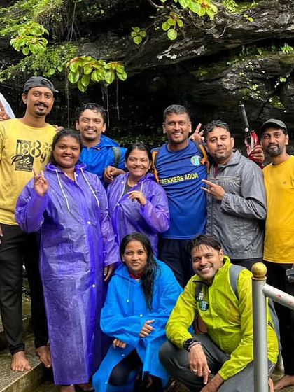 A happy group photo on the steps leading to a cave or waterfall, all smiles in their raincoats.