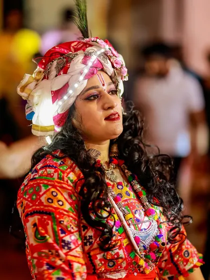 A close-up of a dancer in a traditional turban with LED lights, her expression serene amidst the high-energy celebration.