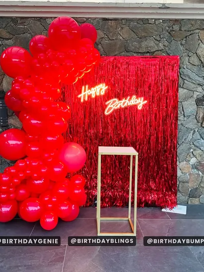 A bold and dramatic statement with a monochrome red balloon garland against a red foil curtain, complete with a "Happy Birthday" neon sign.