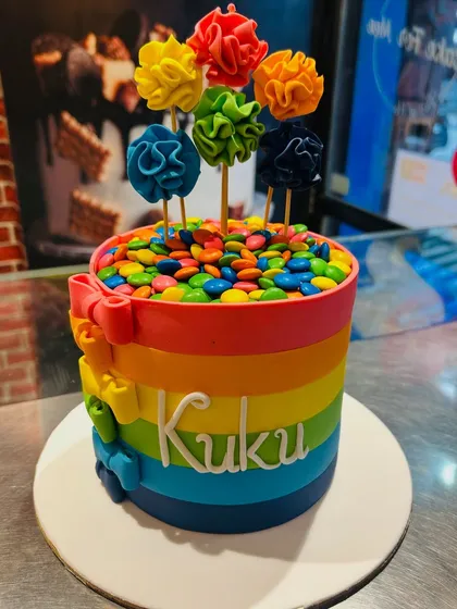 A vibrant rainbow cake topped with colorful gems and fondant flowers. This cheerful design is perfect for bringing a splash of color to any celebration.