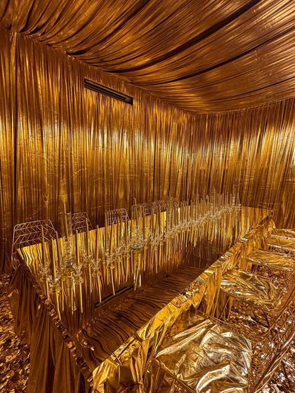 An alternate view of the all-gold dining room, showcasing the complete transformation. The metallic fabric drapes the ceiling and walls, creating a seamless, shimmering cave of opulence for an unforgettable dining experience.