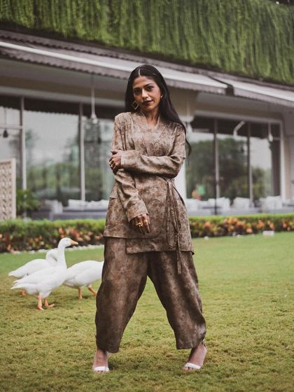 A full-length shot of Anasuya Sengupta in a beautiful garden setting. The natural environment provides a soft, serene backdrop for her stylish ensemble.