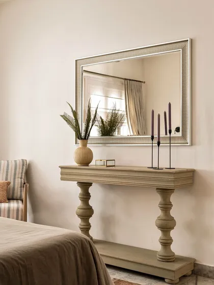 A distressed-finish console table and an ornate mirror add to the vintage charm of the master bedroom. These carefully selected pieces contribute to the room's story, making it feel curated over time.