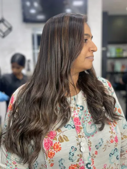 A happy client showing off her new hairstyle, featuring natural-looking highlights and soft waves.