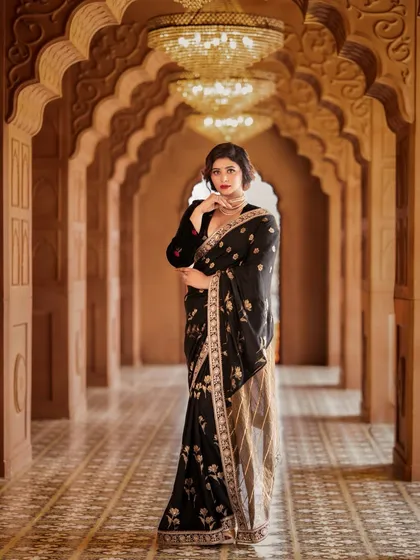 A regal and opulent look for a calendar shoot, featuring a model in a black and gold embroidered saree. The grand arches and chandeliers in the background enhance the luxurious feel.