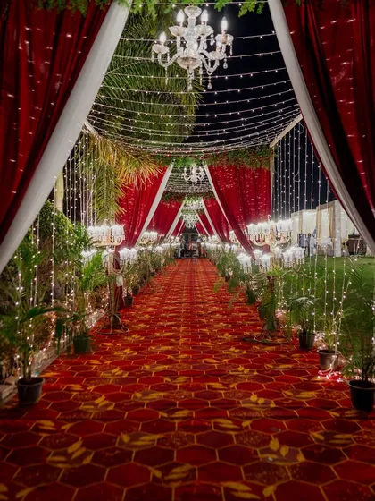 The entrance to a royal affair should be nothing short of majestic. We designed this breathtaking walkway with dramatic red and white drapery, a grand patterned carpet, and a cascade of fairy lights and chandeliers, setting a tone of regal elegance from the very first step.