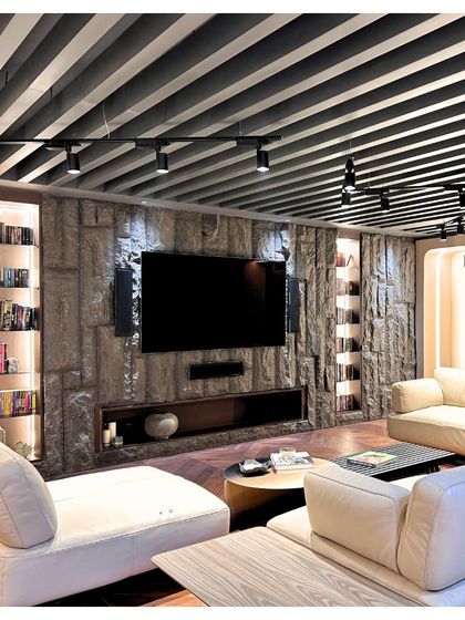 The media lounge in the Palm Springs Villa combines comfort with high-end design. The textured stone wall provides a dramatic backdrop for the screen, while the slatted ceiling and integrated shelving create a cohesive and immersive entertainment space.